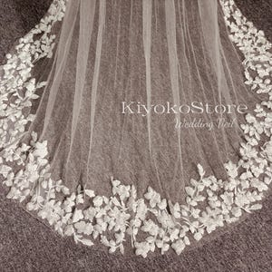 May include: A white wedding veil with a delicate floral lace trim. The lace features a repeating pattern of small leaves and flowers. The veil is made of soft tulle and is perfect for a bride looking for a romantic and elegant look.