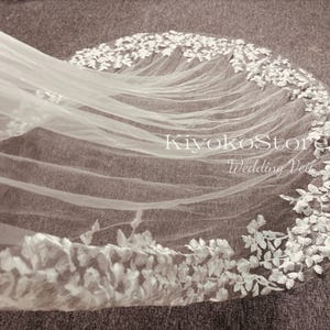 May include: White wedding veil with a delicate floral lace trim. The veil is made of soft tulle and features a scalloped edge.