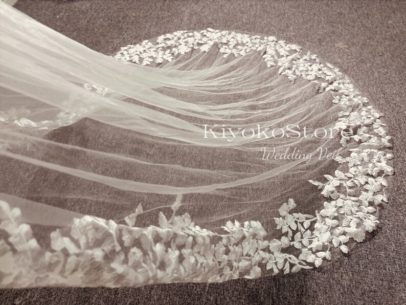 May include: White wedding veil with a delicate floral lace trim. The veil is made of soft tulle and features a scalloped edge.