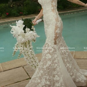 Pu&ograve; includere: Un abito da sposa lungo in pizzo bianco con scollo a cuore, pannelli laterali trasparenti e gonna svasata, caratterizzato da ricami floreali e paillettes. Il testo KiyokoStore Custom wedding dress &egrave; visibile nell'immagine.