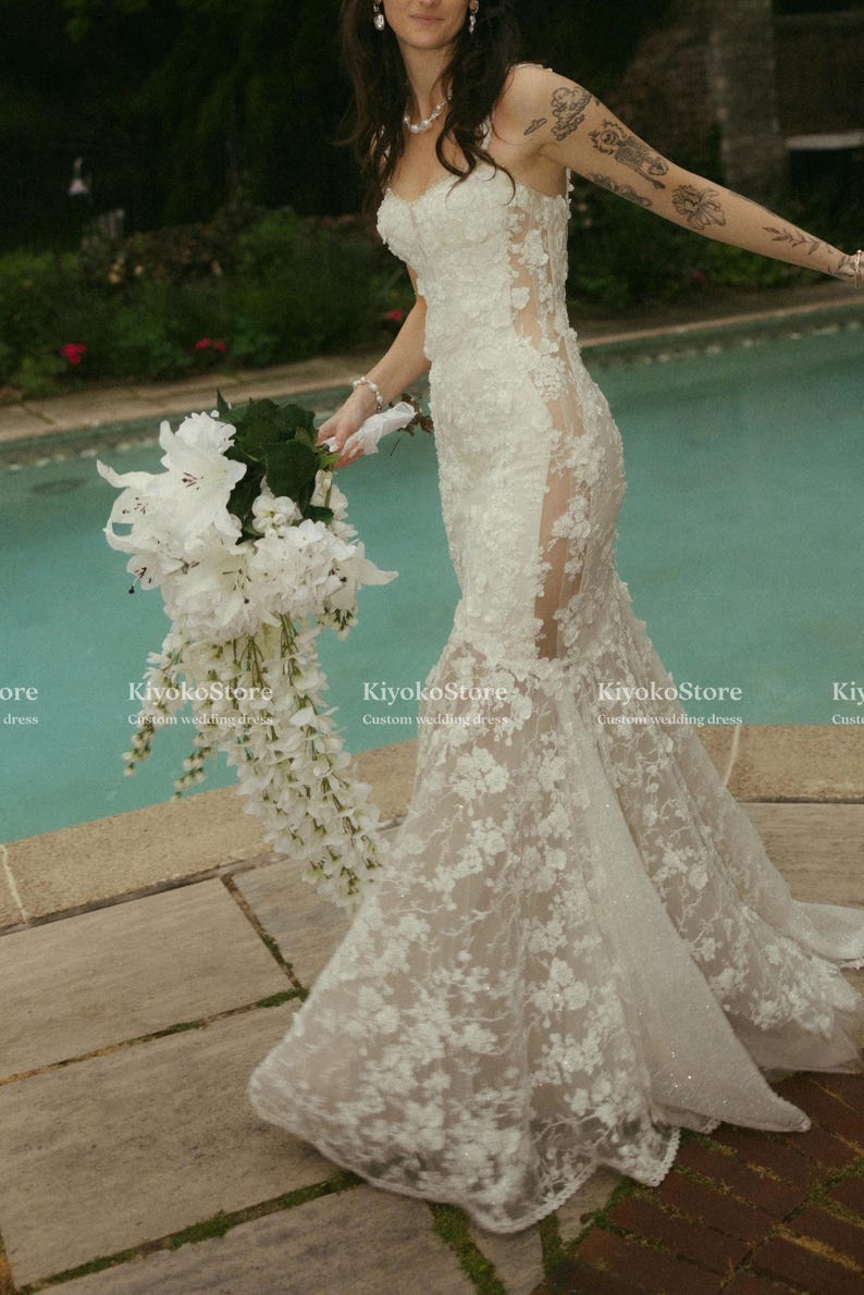 Pu&ograve; includere: Un abito da sposa lungo in pizzo bianco con scollo a cuore, pannelli laterali trasparenti e gonna svasata, caratterizzato da ricami floreali e paillettes. Il testo KiyokoStore Custom wedding dress &egrave; visibile nell'immagine.