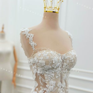 Pu&ograve; includere: Un corpetto senza maniche con una base color carne, decorato con intricati ricami floreali in pizzo bianco e piccole perle. Il capo presenta uno scollo a cuore, ampie spalline in pizzo e un design a corsetto strutturato con cuciture.