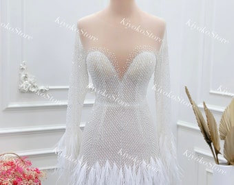 May include: A white mini dress with long sleeves and a feather trim. The dress is covered in sequins and has a plunging neckline.