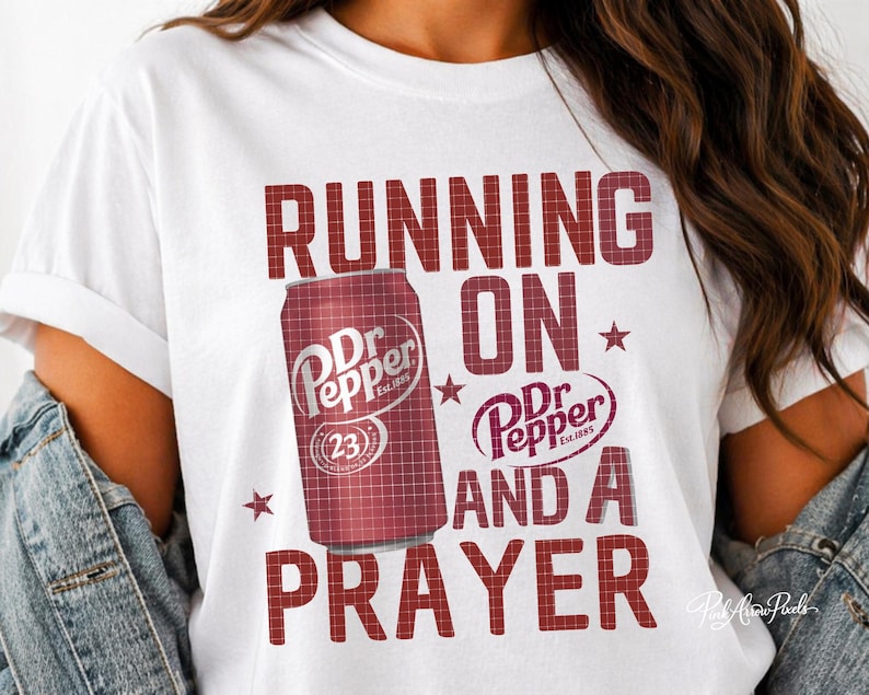 May include: White t-shirt with a maroon graphic featuring a Dr. Pepper can and the text "RUNNING ON Dr Pepper AND A PRAYER". The Dr. Pepper can is red with white text and the number 23.