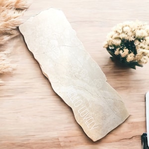 May include: A light beige rectangular tray with a rough, textured surface. The tray has a white inscription that reads "HELLO LOVELY". The tray is on a light brown wooden surface with dried flowers and a tablet.