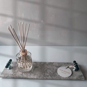 May include: A rectangular gray marble tray with a clear glass diffuser bottle and wooden reeds. The tray has two black and silver handles and a white tag that reads "FIOR DESIGNS HOME DECOR".