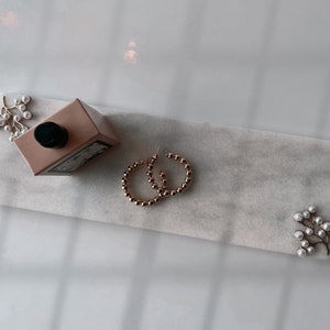 May include: A white marble tray with gold-toned hoop earrings, a bottle of perfume, and two pearl sprigs.