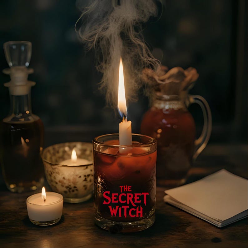 May include: A lit candle in a glass with the text "THE SECRET WITCH" in red. Other candles, a glass bottle, and a pitcher are also on the wooden surface. Smoke rises from the lit candle.