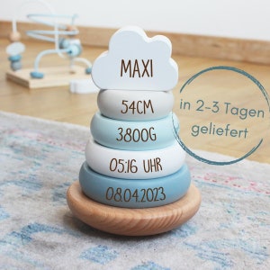 Könnte beinhalten: Ein blaues und weißes Holz-Stapelspielzeug mit dem Namen "MAXI" auf dem obersten Teil. Das Spielzeug enthält auch die Maße "54CM", "3800G", "05:16 UHR" und "08.04.2023".