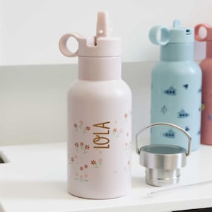 May include: A light pink water bottle with a flip-top lid and a floral design. The word "LOLA" is printed in gold. Other water bottles in blue and pink are visible in the background.