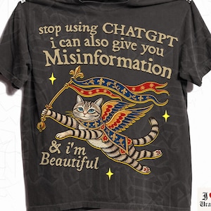 Może przedstawiać: Ciemnoszary t-shirt z grafiką skrzydlatego kota pręgowanego trzymającego sztandar. Tekst głosi: stop using CHATGPT i can also give you Misinformation & i'm Beautiful. Kot ma na sobie niebiesko-złotą pelerynę z motywami lilii heraldycznej.
