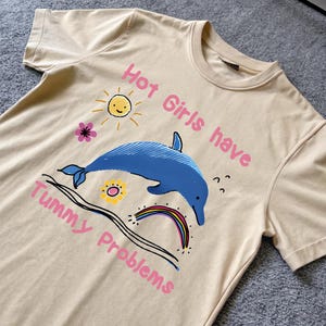 Las chicas atractivas tienen problemas de estómago - Camiseta unisex con meme de dibujo de un delfín divertido