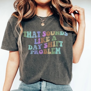 May include: A dark grey t-shirt with the text "THAT SOUNDS LIKE A DAY SHIFT PROBLEM" in colourful letters.