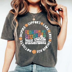 May include: A dark gray t-shirt with a colorful circle graphic that says "Teacher of Students with Visual Impairments". The graphic is surrounded by the words "Inspire, Motivate, Encourage, Love, Care, Support" in a circle.