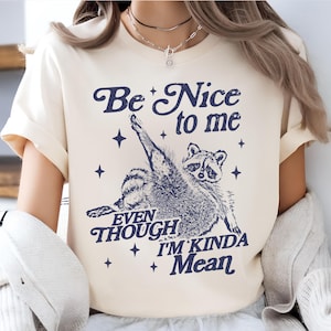 May include: A cream colored t-shirt with a blue graphic of a raccoon with the text "Be Nice to me Even Though I'm Kinda Mean".