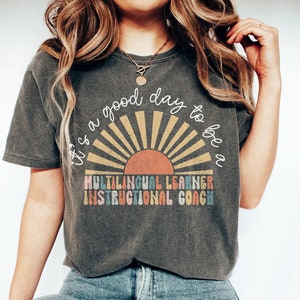 Könnte beinhalten: Ein graues T-Shirt mit einer Retro-Sonnengrafik und dem Text "It's a good day to be a Multilingual Learner Instructional Coach".