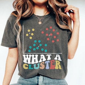 May include: A gray t-shirt with a scatter plot graphic and the text "WHAT A CLUSTER" in rainbow colors.