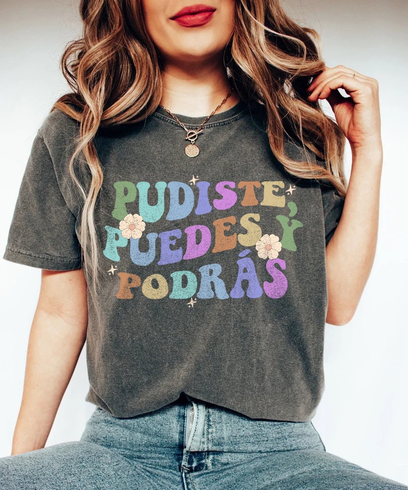 May include: A dark gray t-shirt with the text "PUDISTE, PUEDES Y PODR&Aacute;S" in rainbow colors with flower accents.