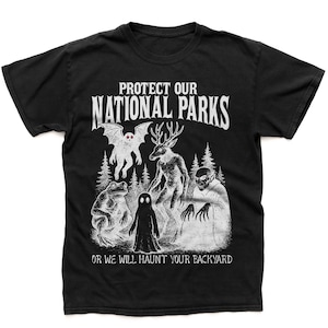 May include: Black t-shirt with a white graphic featuring the text "PROTECT OUR NATIONAL PARKS" above a spooky illustration of forest creatures. The phrase "OR WE WILL HAUNT YOUR BACKYARD" is printed below the illustration.