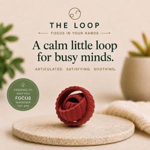 May include: A dark red, spherical, articulated fidget toy with a ribbed texture. The text reads: THE LOOP, FOCUS IN YOUR HANDS, A calm little loop for busy minds. ARTICULATED. SATISFYING. SOOTHING. DESIGNED TO HELP YOU FOCUS WHEREVER YOU ARE.