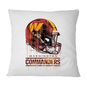 May include: A white cushion featuring a red and gold football helmet with a dripping paint effect. The helmet has a "W" on the side. The text "WASHINGTON COMMANDERS" is below the helmet.