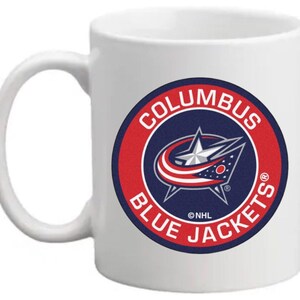 May include: White ceramic coffee mug featuring a blue and red Columbus Blue Jackets NHL logo. The logo depicts a star and a stylised letter C.