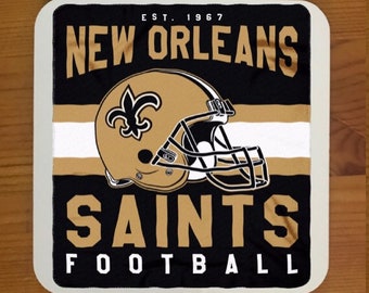 May include: A white square mousepad with a black and gold New Orleans Saints logo. The logo features a football helmet, the team name, and the words "EST. 1967" and "FOOTBALL".