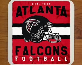 Puede incluir: Un posavasos cuadrado rojo, blanco y negro con las palabras "Atlanta Falcons Football" y el logotipo del equipo, un casco de halcón negro y rojo con un ala roja.