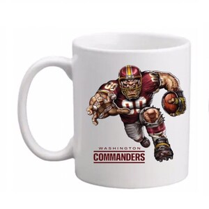 May include: White ceramic coffee mug featuring a cartoon football player in a burgundy and gold uniform. The player is running with the football. The text "WASHINGTON COMMANDERS" is printed below the player.