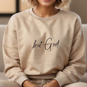 Pu&ograve; includere: Una felpa beige con il testo "but God" scritto in corsivo nero.