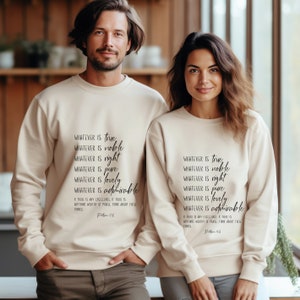 K&ouml;nnte beinhalten: Beigefarbener Crewneck-Pullover mit dem Text "Whatever is true, whatever is noble, whatever is right, whatever is pure, whatever is lovely, whatever is admirable. If there is any excellence, if there is anything worthy of praise, think about these things. Philippians 4:8" in Schwarz gedruckt.