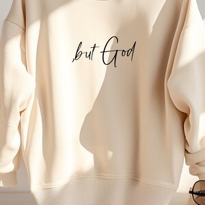 Pu&ograve; includere: Una felpa color crema con il testo "but God" scritto in corsivo nero.