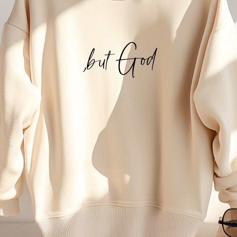 Pu&ograve; includere: Una felpa color crema con il testo "but God" scritto in corsivo nero.