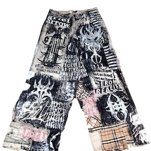 May include: Wide-leg, patchwork denim pants with a distressed, grunge aesthetic. The pants feature a mix of black and white graphics, text, and various fabric patches, including leopard print and plaid. The text includes the words "grief arrow" and "detached from reality."