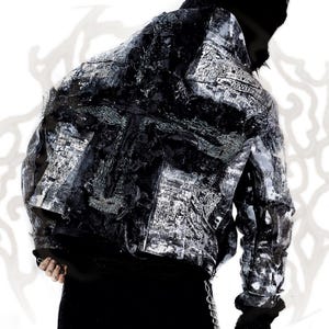 Peut inclure: Une veste noire et blanche à l'aspect vieilli, dotée d'une surface superposée et très texturée avec des bords effilochés et un motif abstrait et chaotique d'éclaboussures d'encre sombre et d'éléments textuels imprimés sur le dos et les manches.