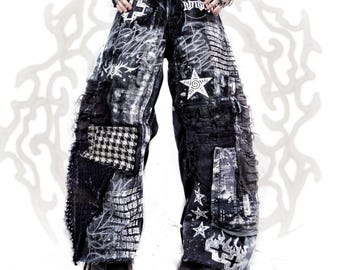 May include: Wide-leg trousers in black and white featuring a distressed, acid-wash finish. The fabric is adorned with white screen-printed graphics including stars, crosses, and graffiti-style text. A black and white houndstooth patch is visible.