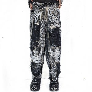May include: Black and white patchwork trousers with a distressed design. The trousers feature various patterns, including skulls, text, and a snake-like print. The trousers have a loose fit and are paired with black platform shoes.