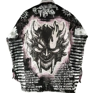 May include: A black and white denim jacket with a pink and white splatter paint design. The jacket features a large black and white graphic of a demon's face with horns and flames. The text "My han ment and tation of angmentation logy, vt ile some paniesker this panies" is printed on the jacket.