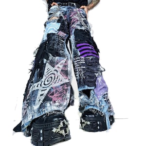 May include: Wide-leg denim trousers featuring heavy distressing, frayed edges, and patchwork elements. The design includes a large white star graphic, purple striped fabric panels, black fabric overlays, and silver chain accents throughout the garment.