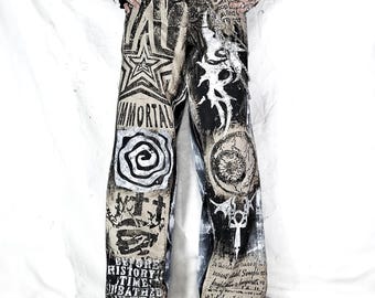 May include: Distressed denim pants with various black and white graphics, including stars, spirals, and text. The pants feature a wide leg design and are paired with black platform shoes. The word "IMMORTAL" is visible on the left leg.