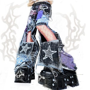 Peut inclure: Pantalon en jean vieilli avec un design patchwork composé de panneaux de tissu noir, bleu et violet, des motifs d'étoiles blanches, des bords effilochés et une chaîne en métal à la taille, associé à des bottes à plateforme noires avec détails métalliques.