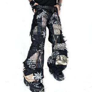 May include: Black denim pants featuring a wide-leg silhouette, distressed frayed edges, and multiple patches including leopard print and metallic fabric. The pants are adorned with white printed text and graphic star motifs throughout the design.