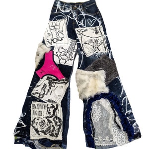 Op de afbeelding: Blauwe denim jeans met verschillende patches en versieringen, waaronder een roze bh, een witte patch met een grafische print, een witte bontpatch en een grijze stofpatch. De jeans hebben een verweerde look en zijn versierd met witte verf.