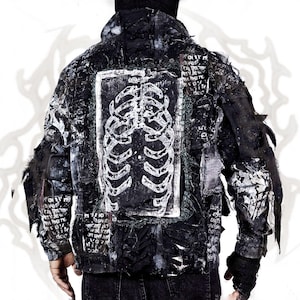 May include: A black jacket featuring a large white ribcage graphic on the back. The garment has a distressed, layered appearance with frayed edges, patches of fabric, and printed text elements throughout the dark, textured surface.