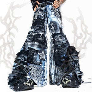 Könnte beinhalten: Weit geschnittene Jeanshose mit verwaschenem Schwarz-Blau-Effekt, geschichteten Stoffstreifen und ausgefransten Kanten. Die Hose ist mit silbernen Ketten, weißen Sternstickereien, einem bedruckten Textfeld und schwarzen Plateauschuhen mit Metallbeschlägen versehen.