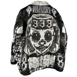 Puede incluir: Chaqueta vaquera negra y blanca con un estampado gráfico de una calavera con un sombrero y el texto "Soul-Draining Penumbra 333".