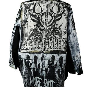 May include: A black and white jacket with a distressed design. The back of the jacket features a large graphic with the word "AFTERLIFE" and "MORE RIOT". The jacket has a tan collar.