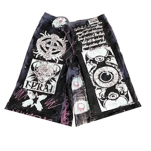 May include: Black and white graphic print shorts with a pink and white design. The shorts feature a variety of images including a skull, an eye, and a creature with wings. The text "FERAL" is printed on the shorts.