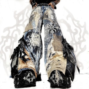 May include: Wide-leg denim pants featuring a distressed patchwork design with frayed edges, layered fabric panels in shades of blue, beige, and black, and metallic hardware accents. The pants include visible stitching, textured fabric patches, and heavy distressing.