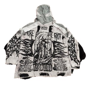 Könnte beinhalten: Ein weißer Kapuzenpullover mit schwarzem und grauem Grafikdruck. Der Druck zeigt eine Figur mit Flügeln, Flammen und dem Text "MORE RIOT VOID".